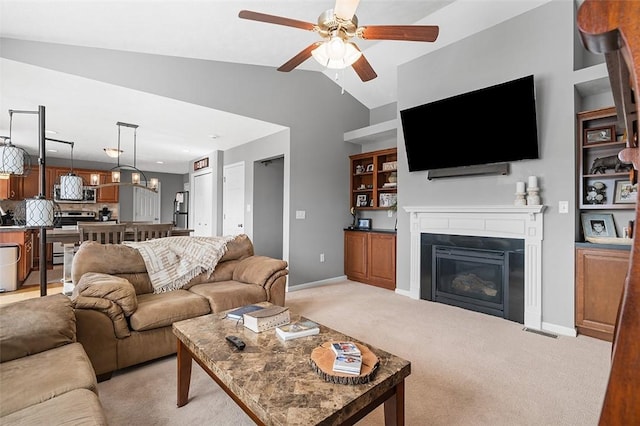 living area with lofted ceiling, light colored carpet, ceiling fan with notable chandelier, baseboards, and a glass covered fireplace