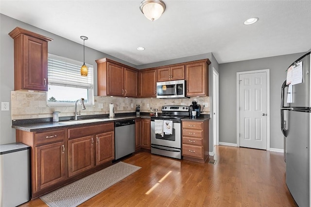 kitchen with dark wood finished floors, stainless steel appliances, dark countertops, tasteful backsplash, and a sink