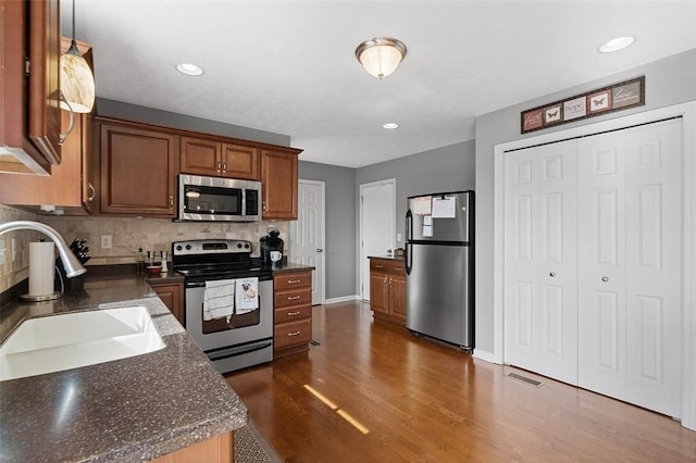 kitchen with stainless steel appliances, a sink, tasteful backsplash, dark countertops, and dark wood finished floors