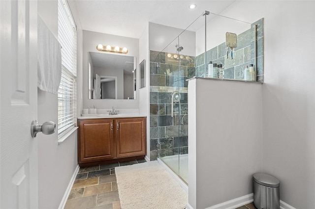 bathroom with baseboards, a shower stall, stone tile floors, and vanity