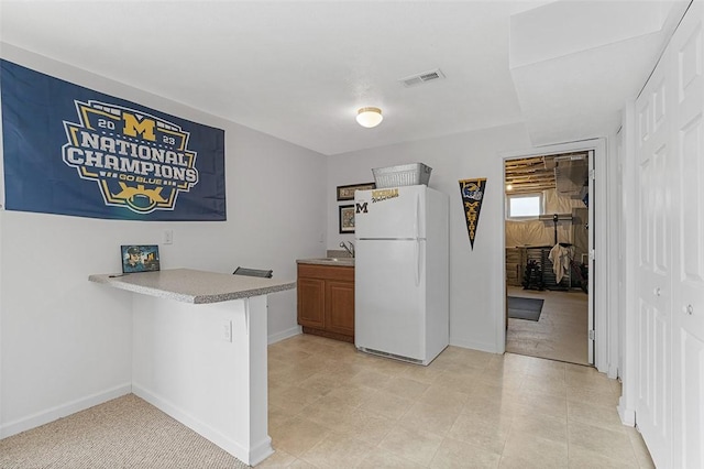 kitchen featuring baseboards, visible vents, freestanding refrigerator, a peninsula, and light countertops