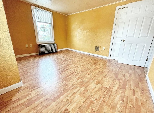 empty room featuring light wood-type flooring, radiator heating unit, ornamental molding, and baseboards