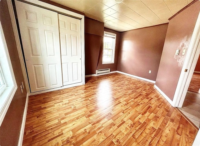 unfurnished bedroom featuring a closet, baseboards, light wood finished floors, and a wall mounted air conditioner