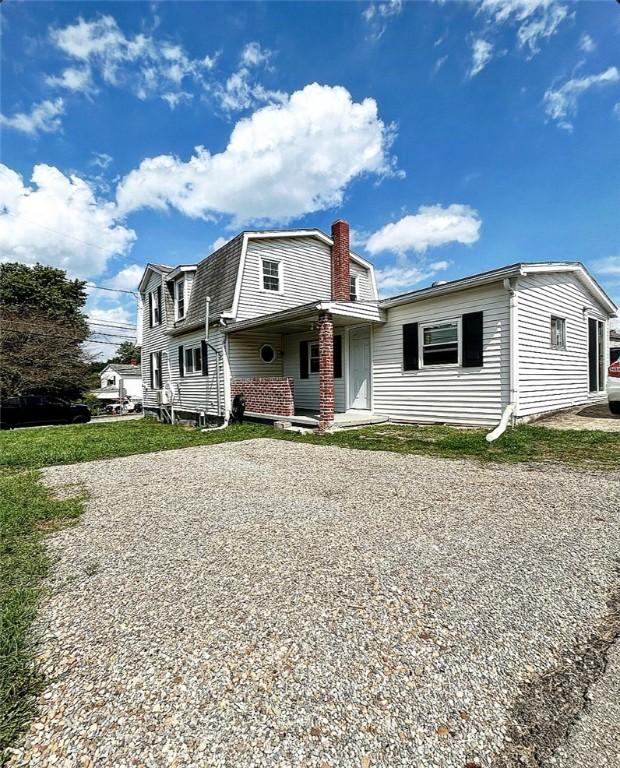 view of front of property featuring gravel driveway, a chimney, and a gambrel roof