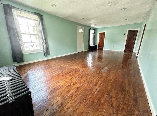 unfurnished living room featuring a textured ceiling, baseboards, and wood finished floors