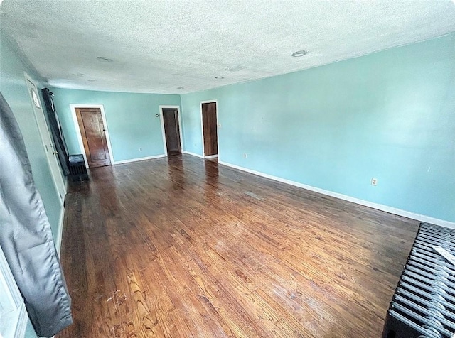 unfurnished room featuring a textured ceiling, dark wood finished floors, and baseboards