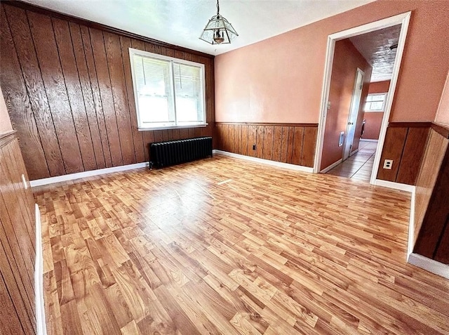 unfurnished dining area with wooden walls, wainscoting, wood finished floors, and radiator