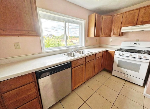 kitchen with light tile patterned floors, white range with gas stovetop, under cabinet range hood, a sink, and dishwasher