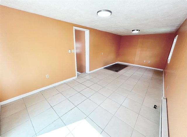 unfurnished room with a textured ceiling, light tile patterned floors, and baseboards