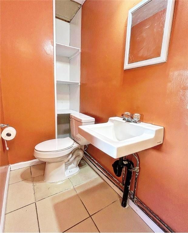 half bath with baseboards, a sink, toilet, and tile patterned floors