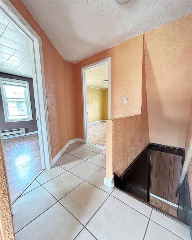 corridor with light tile patterned floors, a baseboard radiator, a textured wall, a textured ceiling, and baseboards