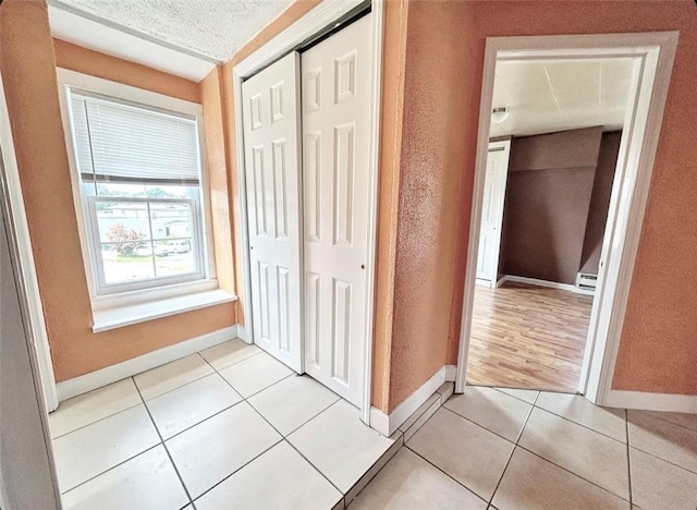 hall featuring light tile patterned floors, a textured wall, a textured ceiling, and baseboards