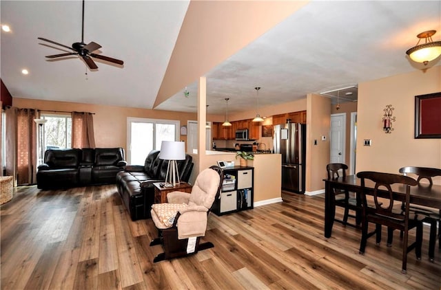 living area with wood finished floors, a ceiling fan, baseboards, vaulted ceiling, and attic access