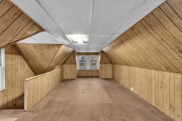 additional living space featuring wood-type flooring, wooden walls, and vaulted ceiling