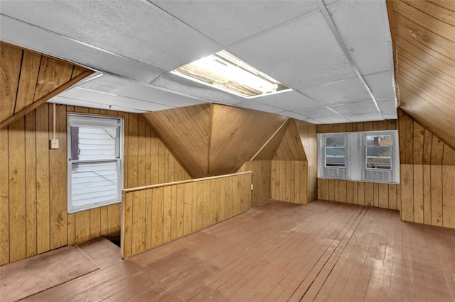 additional living space with lofted ceiling, a wealth of natural light, wood walls, and hardwood / wood-style flooring