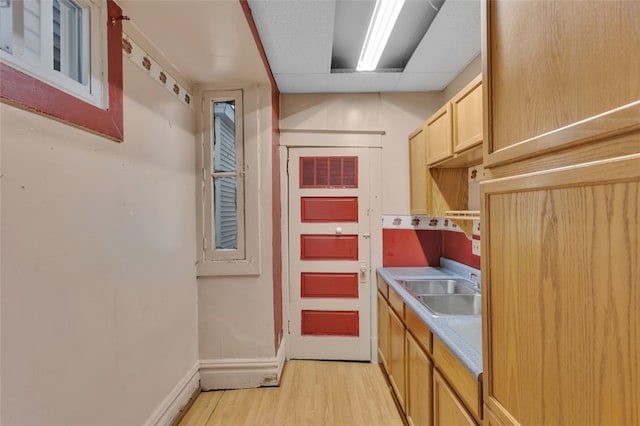 kitchen featuring light countertops, light brown cabinets, a sink, light wood-type flooring, and baseboards