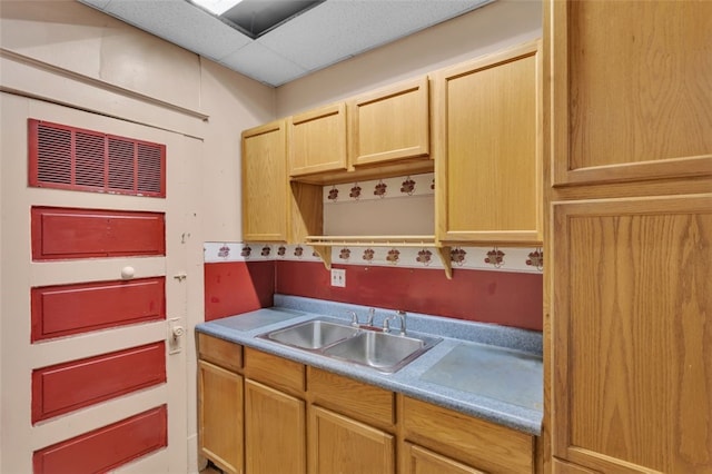 kitchen with light brown cabinets, light countertops, a drop ceiling, and a sink