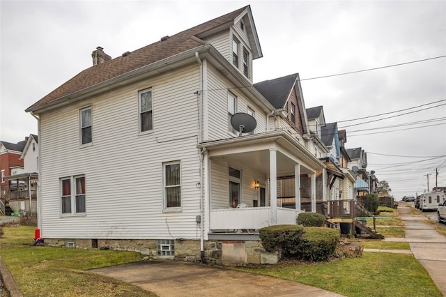 view of side of home featuring a chimney, a porch, and a yard