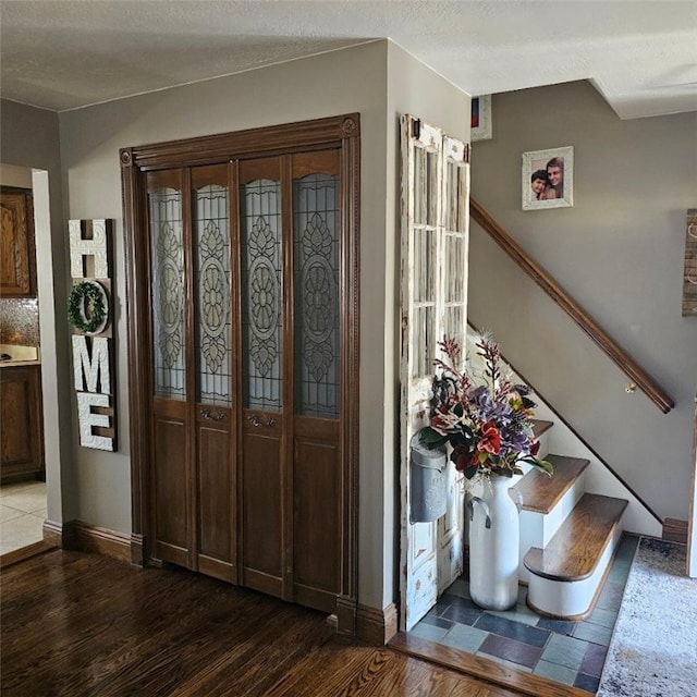 foyer featuring stairs, a textured ceiling, baseboards, and wood finished floors