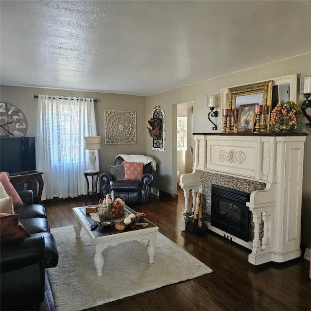 living area with dark wood-style floors, a textured ceiling, and a glass covered fireplace