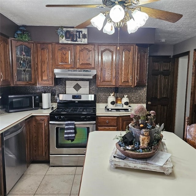 kitchen with stainless steel appliances, light countertops, backsplash, a textured ceiling, and under cabinet range hood