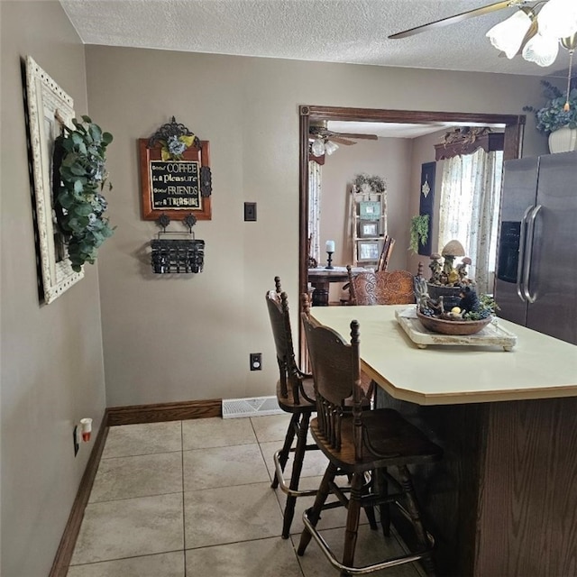 dining area featuring light tile patterned floors, visible vents, baseboards, a ceiling fan, and a textured ceiling