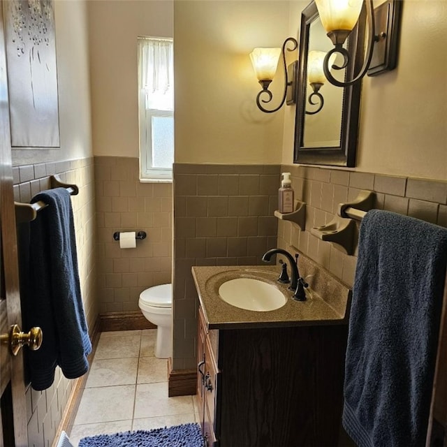 bathroom featuring tile patterned flooring, toilet, vanity, tile walls, and wainscoting