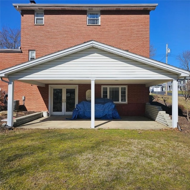 rear view of house with central air condition unit, brick siding, french doors, a lawn, and a patio area