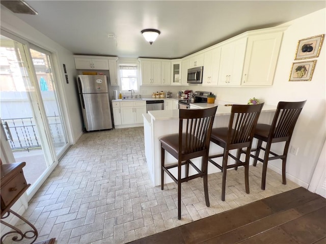 kitchen featuring appliances with stainless steel finishes, glass insert cabinets, a peninsula, light countertops, and a sink