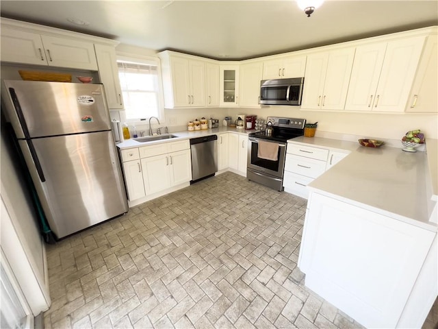 kitchen featuring stainless steel appliances, a sink, light countertops, brick patterned floor, and glass insert cabinets