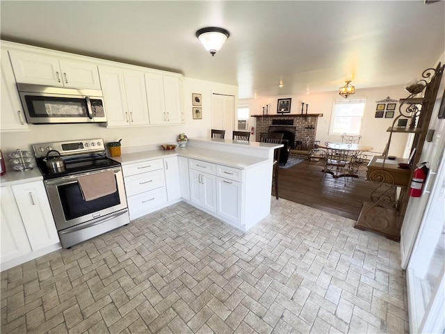 kitchen featuring a peninsula, appliances with stainless steel finishes, light countertops, and white cabinetry