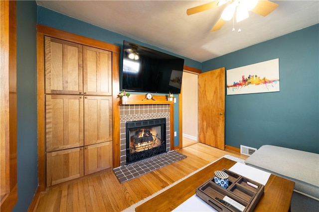 living area featuring wood finished floors, visible vents, baseboards, a ceiling fan, and a tiled fireplace