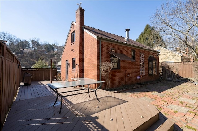 rear view of house with a chimney, fence, outdoor dining area, a deck, and brick siding