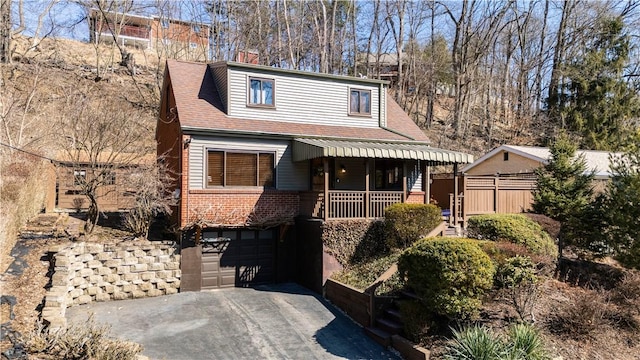 view of front of house featuring driveway, a garage, roof with shingles, a porch, and brick siding