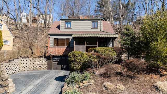 view of front of house featuring aphalt driveway, roof with shingles, an attached garage, a porch, and brick siding