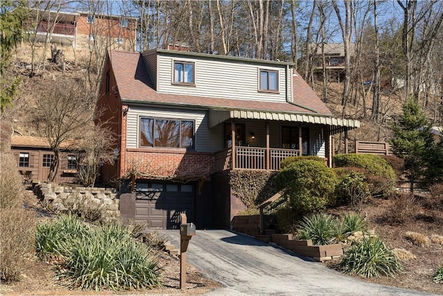 view of front of property featuring a porch, aphalt driveway, a garage, a shingled roof, and brick siding