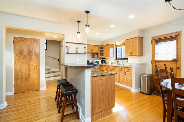 kitchen featuring light wood-style flooring, a kitchen bar, pendant lighting, a sink, and recessed lighting