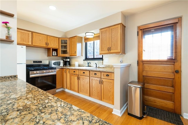 kitchen featuring light wood-type flooring, white appliances, glass insert cabinets, and a sink