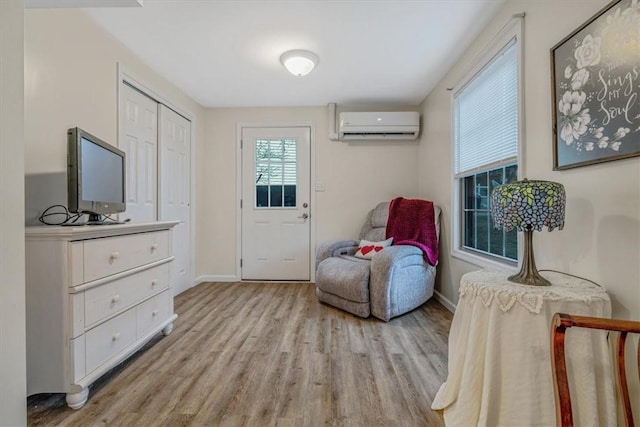 sitting room with an AC wall unit, baseboards, and light wood finished floors