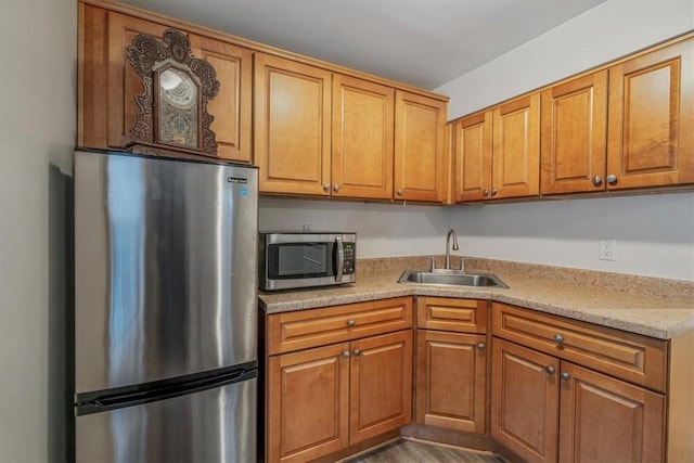 kitchen with appliances with stainless steel finishes, brown cabinets, a sink, and wood finished floors