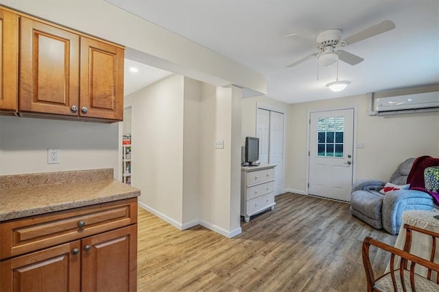 kitchen featuring baseboards, a wall unit AC, brown cabinets, light countertops, and light wood-style floors