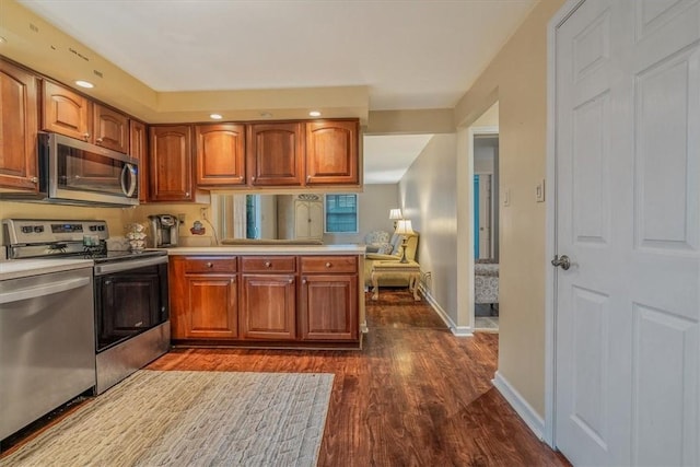 kitchen with stainless steel appliances, a peninsula, light countertops, brown cabinets, and dark wood finished floors