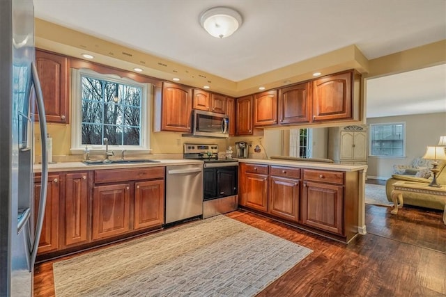 kitchen with stainless steel appliances, a peninsula, dark wood-style flooring, a sink, and open floor plan