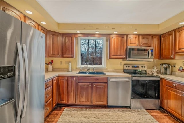 kitchen featuring brown cabinets, wood finished floors, stainless steel appliances, light countertops, and a sink