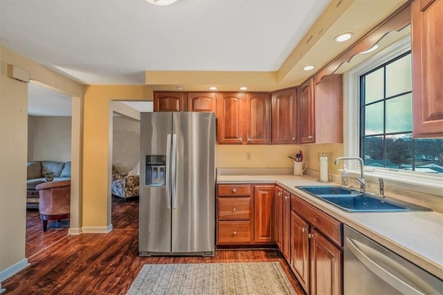 kitchen with dark wood-style flooring, light countertops, appliances with stainless steel finishes, brown cabinetry, and a sink