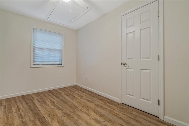 unfurnished room featuring wood finished floors, attic access, and baseboards