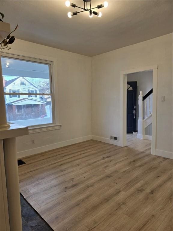 spare room with visible vents, baseboards, an inviting chandelier, stairs, and light wood-style floors