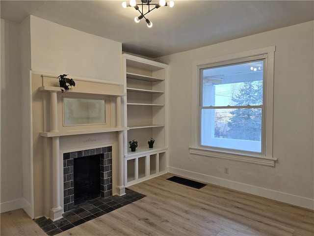 unfurnished living room featuring a tiled fireplace, wood finished floors, visible vents, and baseboards