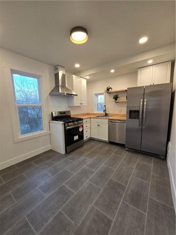 kitchen featuring stainless steel appliances, wall chimney range hood, white cabinetry, and baseboards