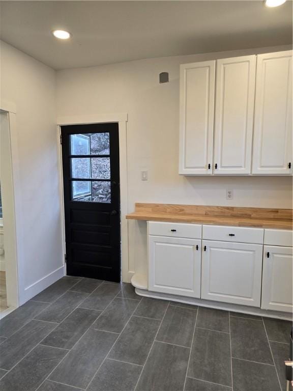 kitchen featuring butcher block countertops, recessed lighting, white cabinets, and baseboards